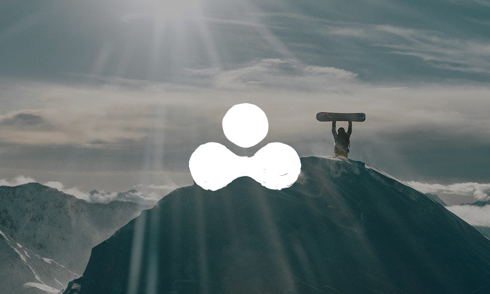Photo of a snowboarder holding their board up in celebration at the top of a snowy mountain. There is an icon on top of the image.