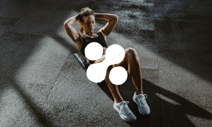 Photo of a woman completing an ab routine in a modern gym. There is an icon on top of the image.
